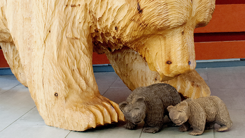 A large wooden sculpture of a bear leaning down towards two small wooden bears standing in front of it.